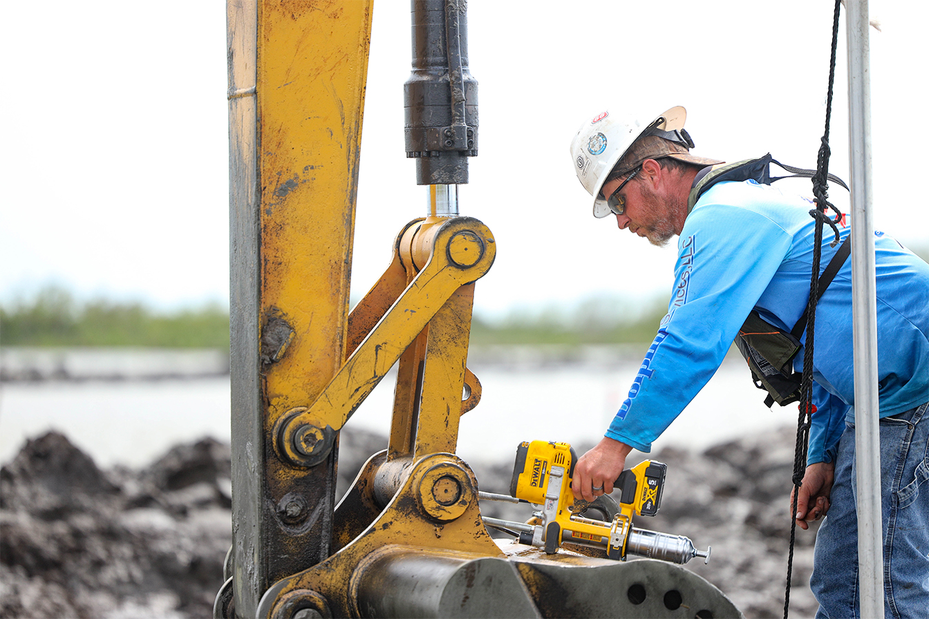 A man wearing a hard hat using a tool to work on an oil rig
